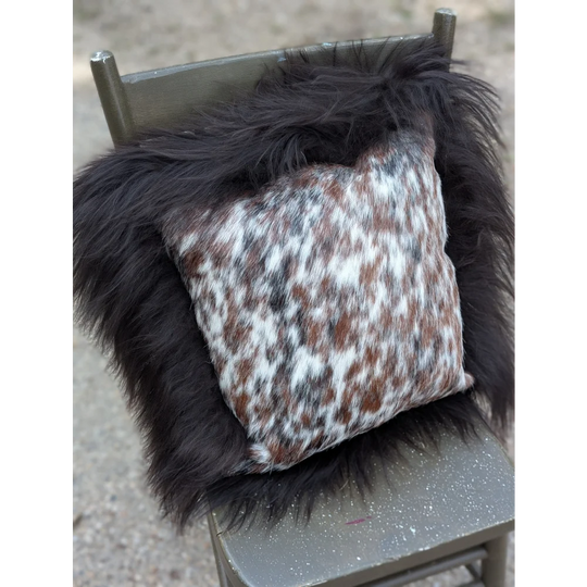A cozy square pillow with natural cowhide speckled cowhide pattern framed by plush black long wool faux fur