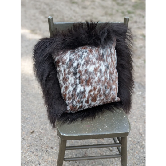 A cozy square pillow with natural cowhide speckled brown white and black pattern framed by plush dark long wool fur