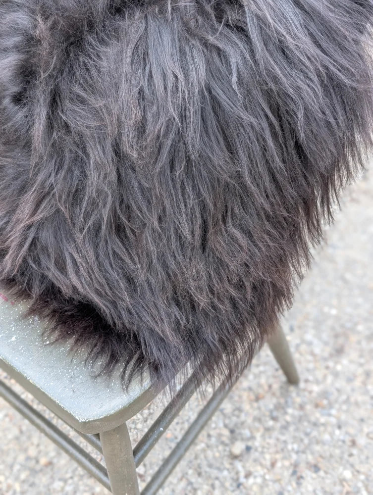 A plush dark gray faux fur throw with long wool strands draped over a metal chair inspired by natural cowhide