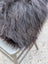 A plush dark gray faux fur throw with long wool strands draped over a metal chair inspired by natural cowhide