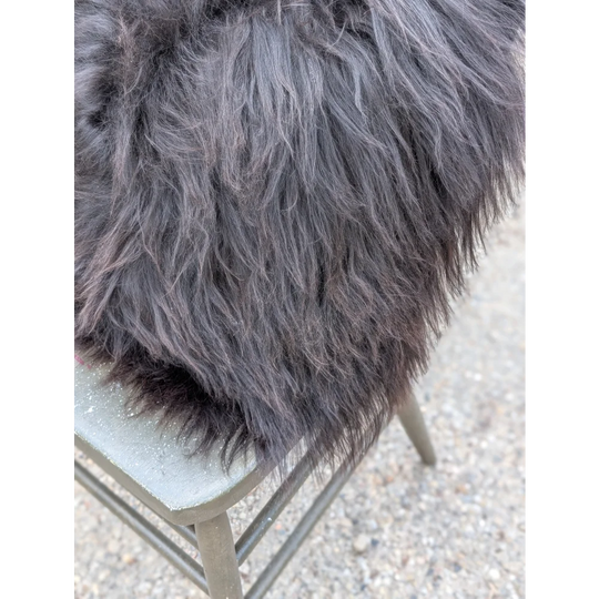 A plush dark gray faux fur throw with long wool strands draped over a metal chair inspired by natural cowhide