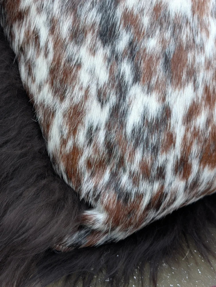 A plush pillow upholstered in natural cowhide with a speckled white and brown pattern perfect for long wool lovers