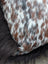 A plush pillow upholstered in natural cowhide with a speckled white and brown pattern perfect for long wool lovers