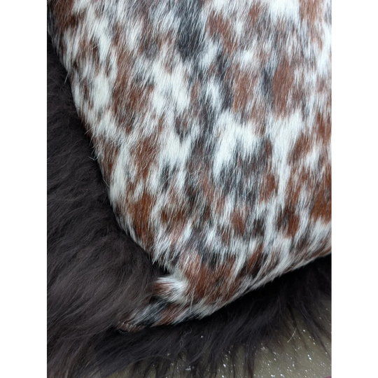 A plush pillow upholstered in natural cowhide with a speckled white and brown pattern perfect for long wool lovers