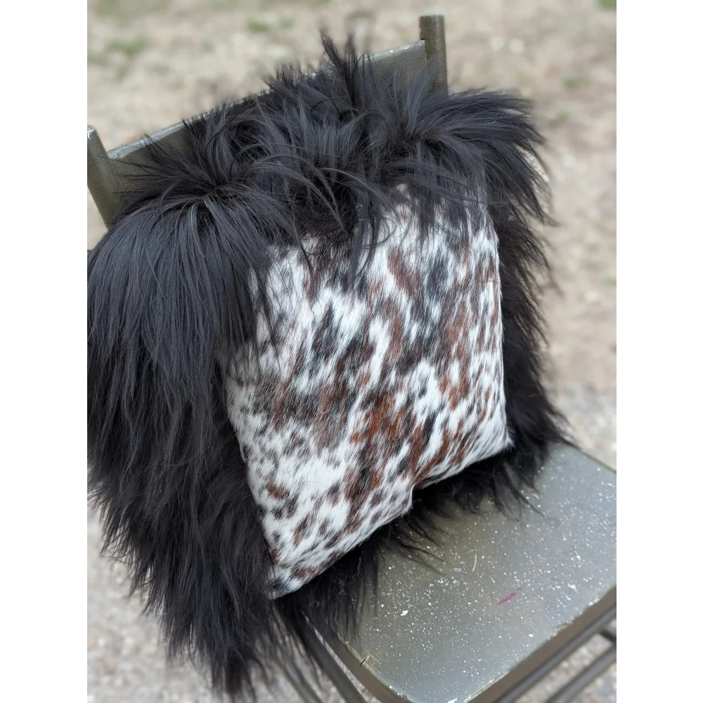 A plush black fur-trimmed pillow with natural cowhide in white brown and gray speckled pattern perfect for cozy decor