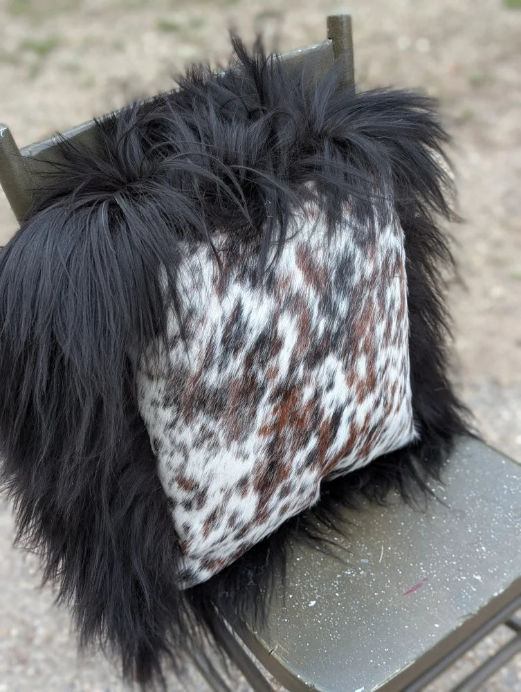 A plush black fur-trimmed pillow with natural cowhide in white brown and gray speckled pattern perfect for cozy decor