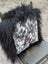A plush black fur-trimmed pillow with natural cowhide in white brown and gray speckled pattern perfect for cozy decor