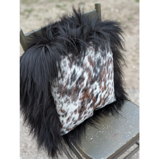 A plush black fur-trimmed pillow with natural cowhide in white brown and gray speckled pattern perfect for cozy decor