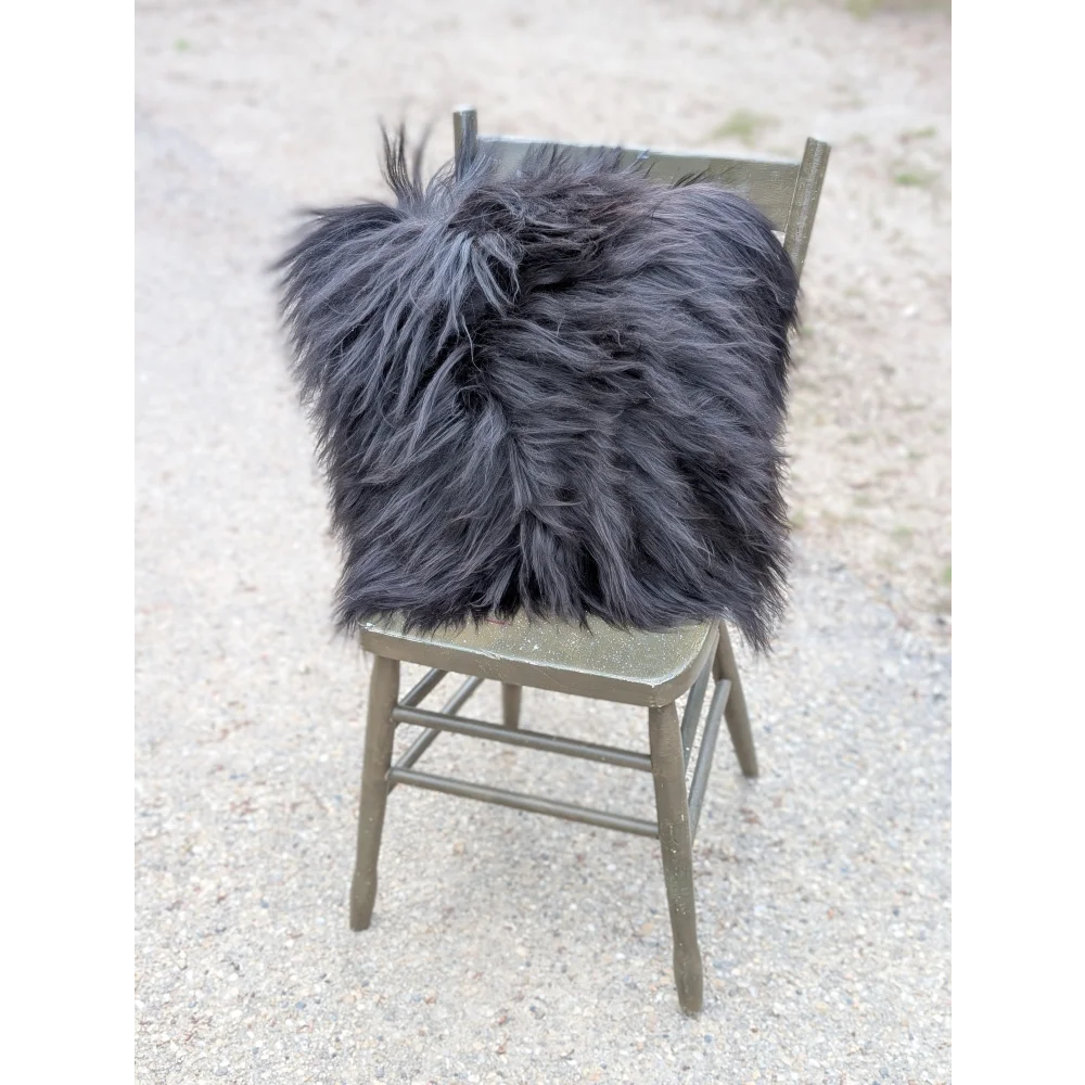 A plush dark gray faux fur throw pillow with long wool texture on olive green wooden chair natural cowhide style