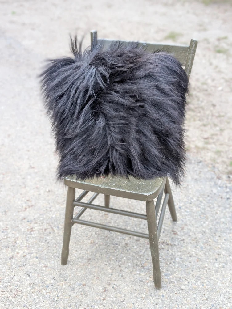 A plush dark gray faux fur throw pillow with long wool texture on olive green wooden chair natural cowhide style