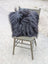 A plush dark gray faux fur throw pillow with long wool texture on olive green wooden chair natural cowhide style