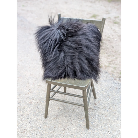 A plush dark gray faux fur throw pillow with long wool texture on olive green wooden chair natural cowhide style