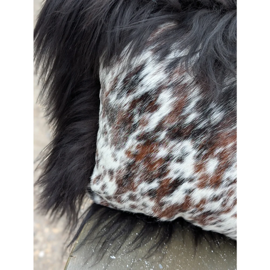 A plush rectangular cushion in natural cowhide with white and brown spots framed by long wool black faux fur trim