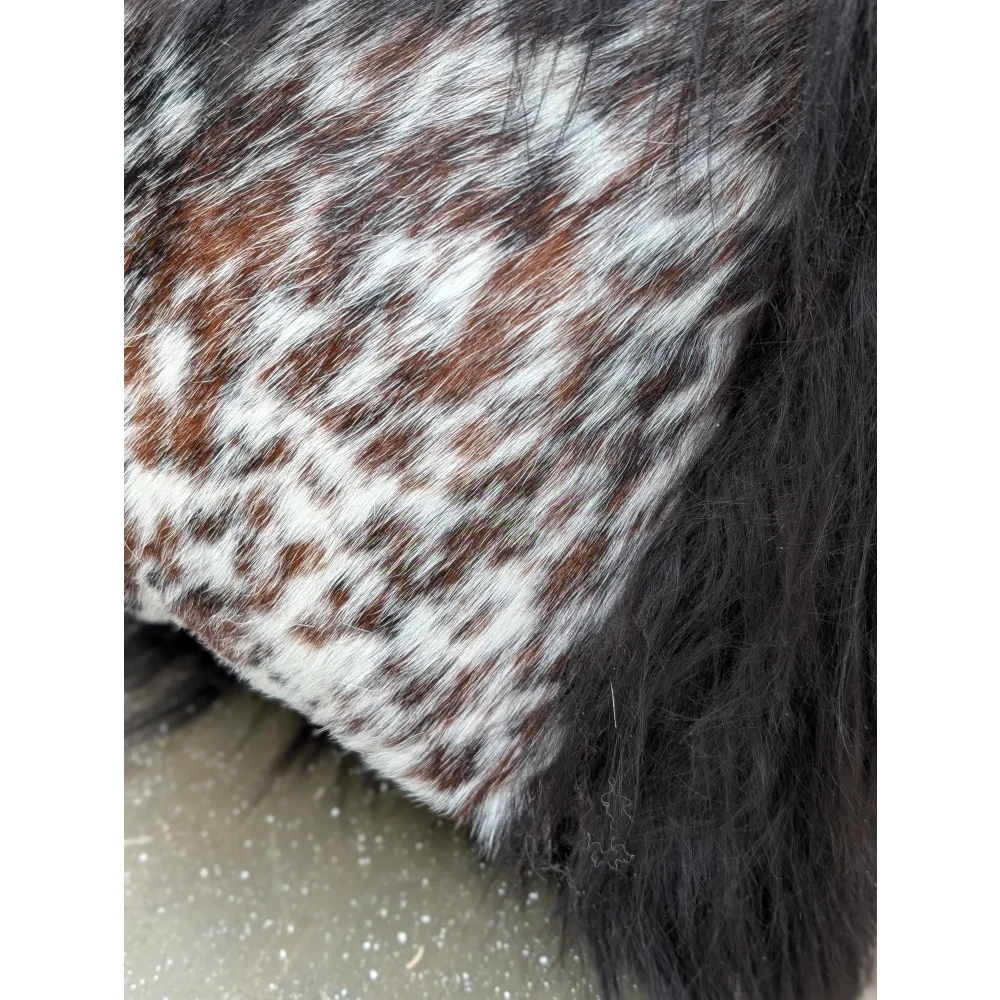 A plush faux fur throw blanket with brown and white spotted pattern featuring natural cowhide and long wool fibers