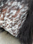 A plush faux fur throw blanket with brown and white spotted pattern featuring natural cowhide and long wool fibers