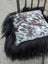 A plush square cushion in natural cowhide with white and brown speckles and long wool black icelandic trim