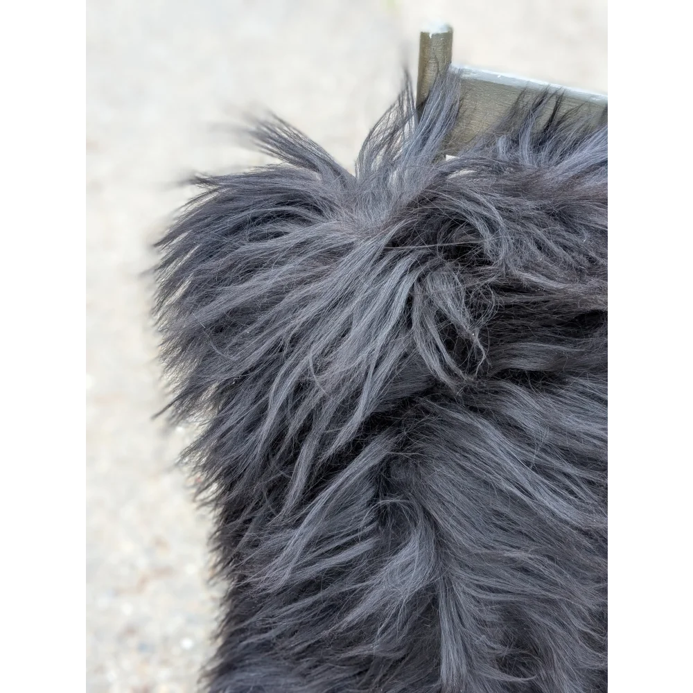A close-up of a natural black icelandic dog tail with long wool fur being gently groomed, paired with speckled cowhide