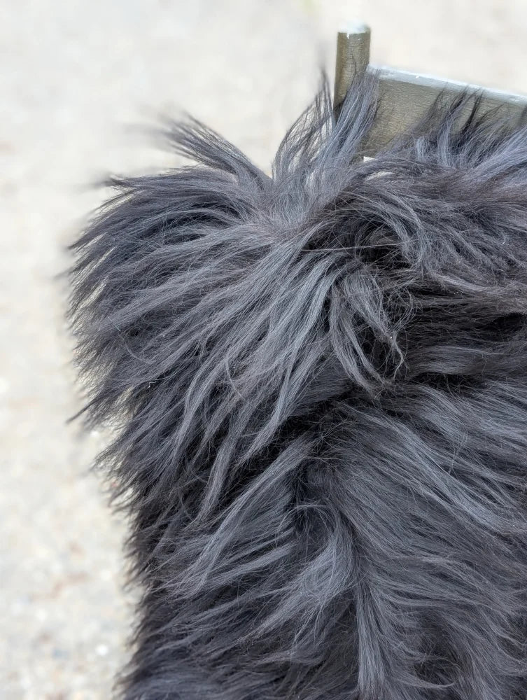 A close-up of a natural black icelandic dog tail with long wool fur being gently groomed, paired with speckled cowhide