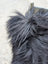 A close-up of a natural black icelandic dog tail with long wool fur being gently groomed, paired with speckled cowhide