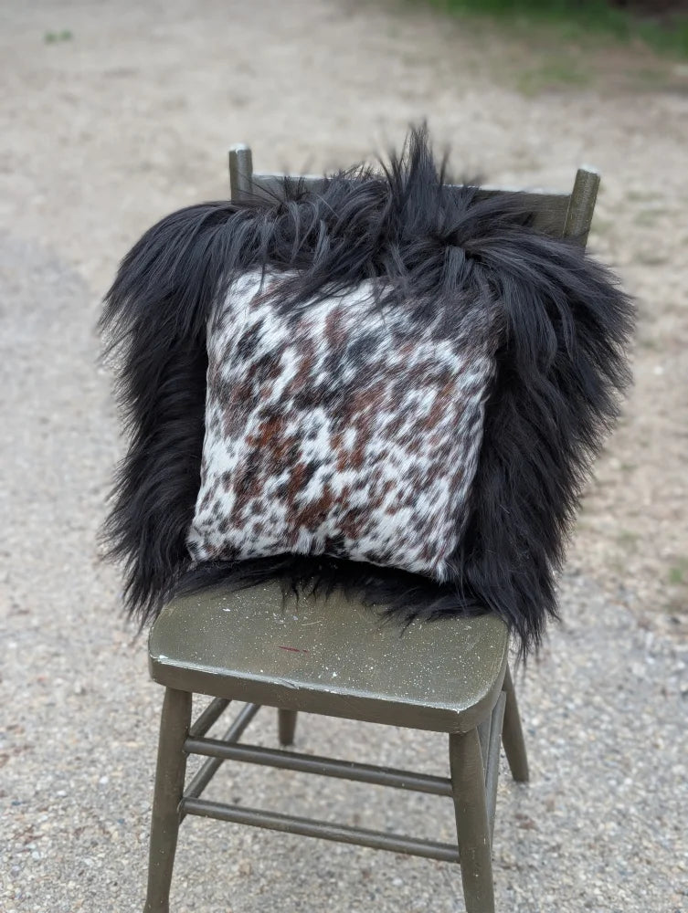 Black and white natural cowhide pillow with fluffy black long wool trim from speckled cowhide and natural black icelandic