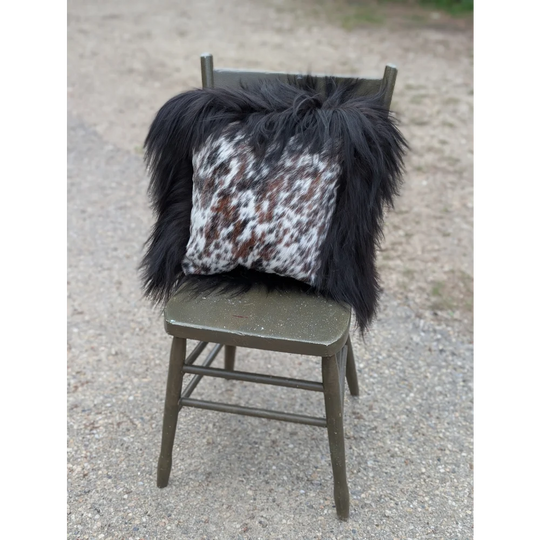 Black and white natural cowhide pillow with speckled pattern and thick long wool black Icelandic fur trim