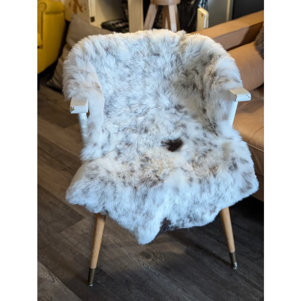 A plush white and gray spotted icelandic sheepskin throw with short wool draped over a vintage wooden chair