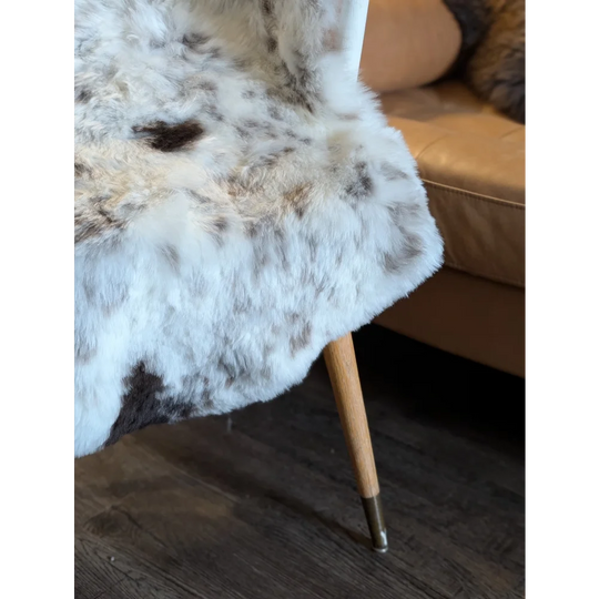 A plush white and gray spotted icelandic sheepskin throw with short wool draped over a wooden-legged chair