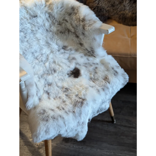 A plush white and gray speckled icelandic sheepskin throw with short wool draped over a wooden chair