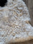 A plush beige and white icelandic sheepskin rug with short wool and natural curly texture measuring 39 by 25.5 inches