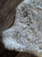 A soft curly gray and white medium spotted icelandic sheepskin rug with short wool on dark wooden floor