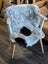 A cozy medium spotted icelandic sheepskin with natural gray and black short wool draped over a white wooden chair