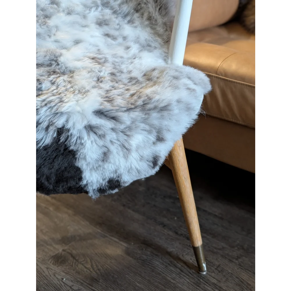 A plush gray and white medium spotted icelandic sheepskin with short wool draped over a wooden chair leg