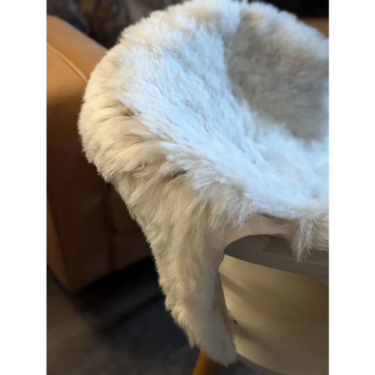 A plush white medium spotted icelandic sheepskin throw with short wool draped over a chair edge