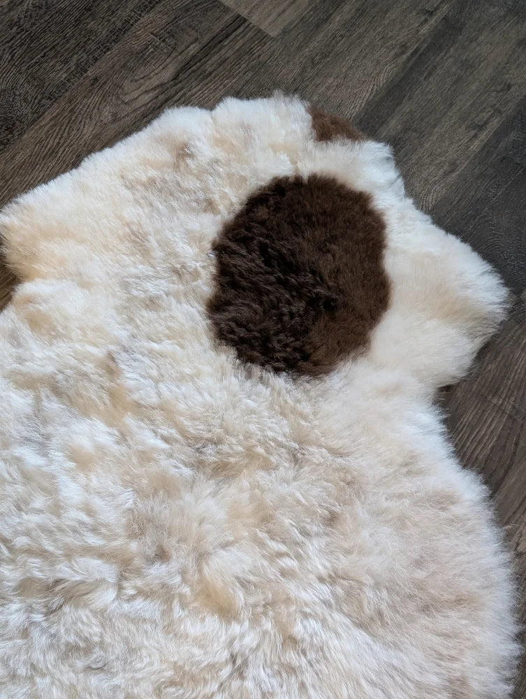 A plush white icelandic sheepskin rug with a dark brown spot made of short wool measuring 40.5 by 29 inches