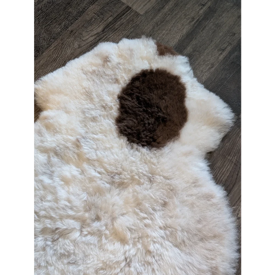 A plush white icelandic sheepskin rug with a dark brown spot made of short wool measuring 40.5 by 29 inches