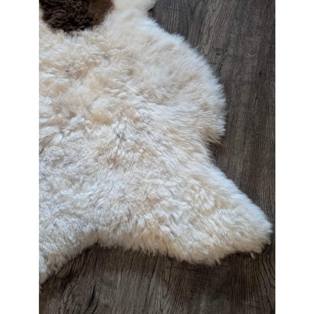 Cream-colored fluffy icelandic sheepskin rug with natural edge made of short wool on dark wood floor