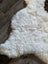 A plush off-white medium spotted icelandic sheepskin rug with soft curly short wool on dark wood floor