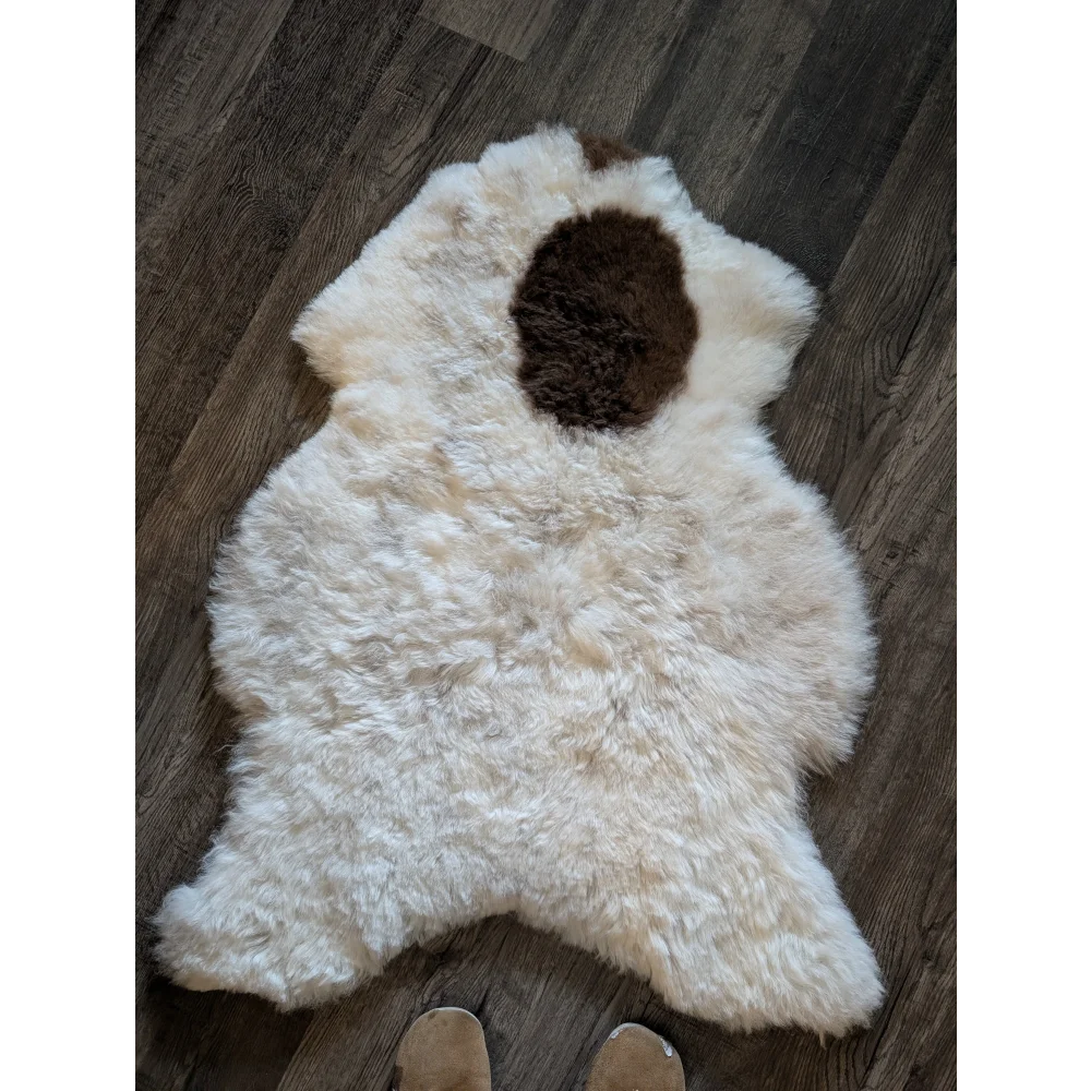 A fluffy white icelandic sheepskin with a brown patch made of short wool on a wooden floor spot12 medium size