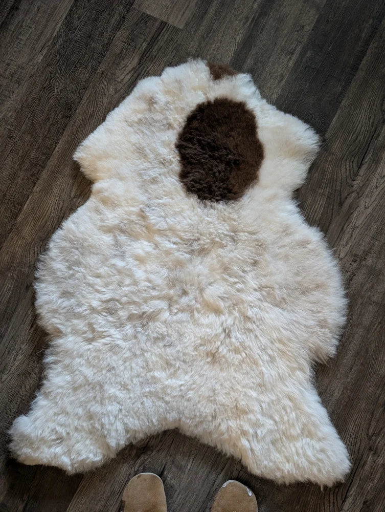 A fluffy white icelandic sheepskin with a brown patch made of short wool on a wooden floor spot12 medium size