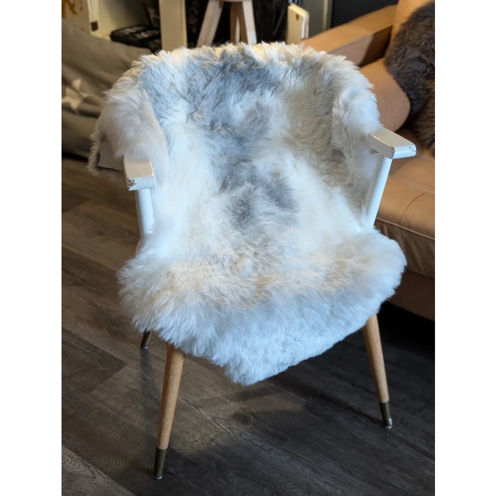 A cozy white and gray medium spotted icelandic sheepskin short wool throw draped over a mid-century modern chair