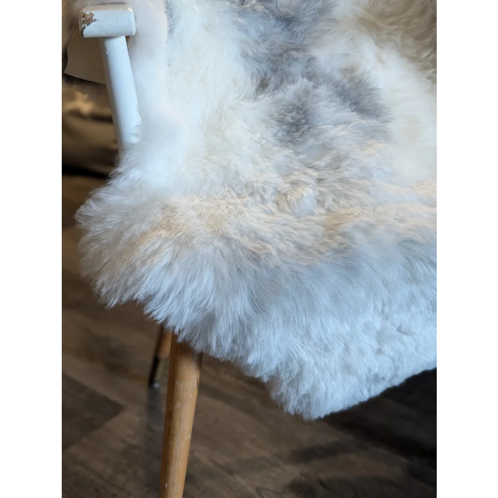 A plush white and gray medium spotted icelandic sheepskin rug with short wool draped over the back of a chair