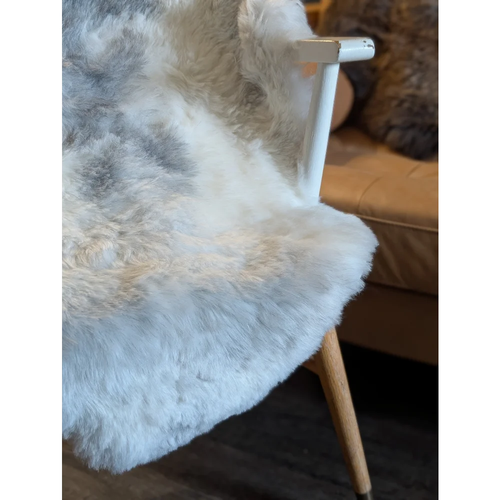 A plush white and gray icelandic sheepskin throw with short wool draped over a modern chair with wooden legs
