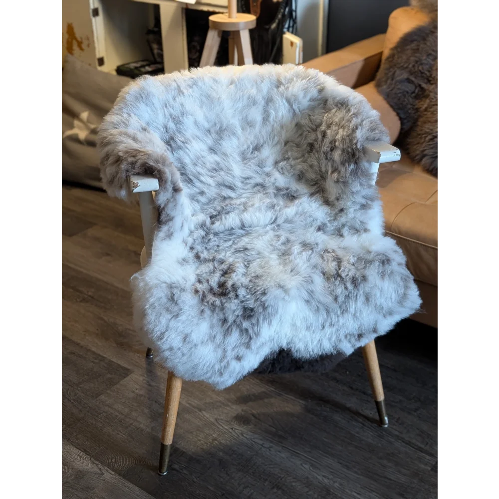 A cozy gray and white medium spotted icelandic sheepskin short wool throw draped over a mid-century modern chair