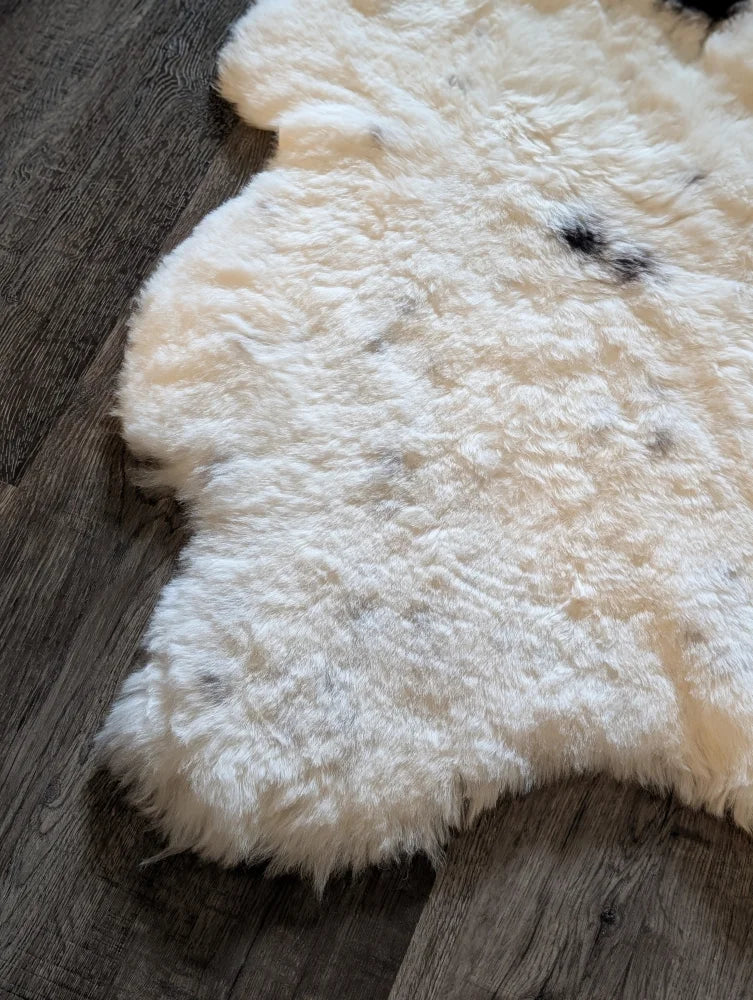 A plush off-white icelandic sheepskin rug with natural black and gray markings and short wool on dark wood floor