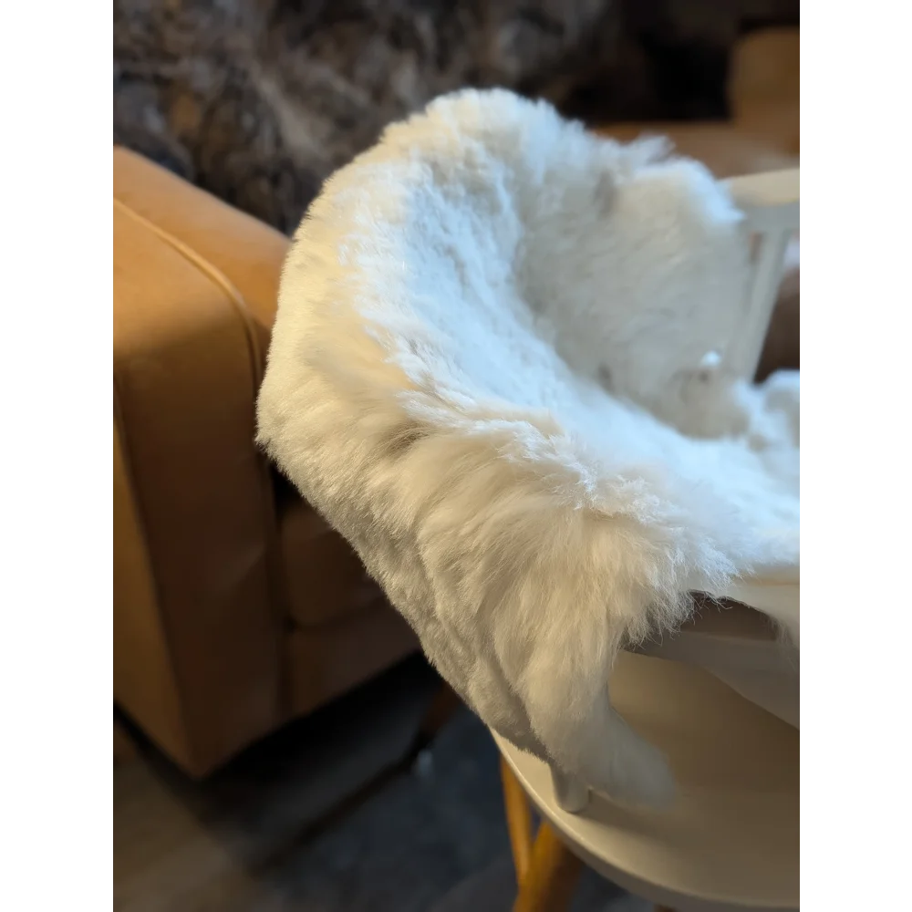 A plush white icelandic sheepskin throw with short wool draped over the edge of a light-colored table