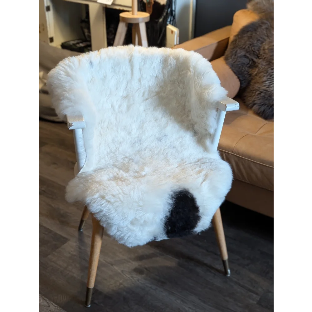 White spotted icelandic sheepskin throw with short wool draped over wooden chair with metal legs