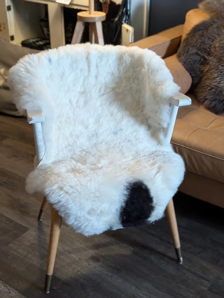 White spotted icelandic sheepskin throw with short wool draped over wooden chair with metal legs