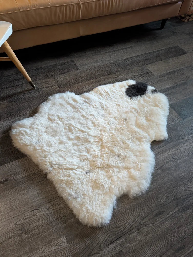 A fluffy white icelandic sheepskin rug with short wool and a black spot on dark wood flooring spot18 medium