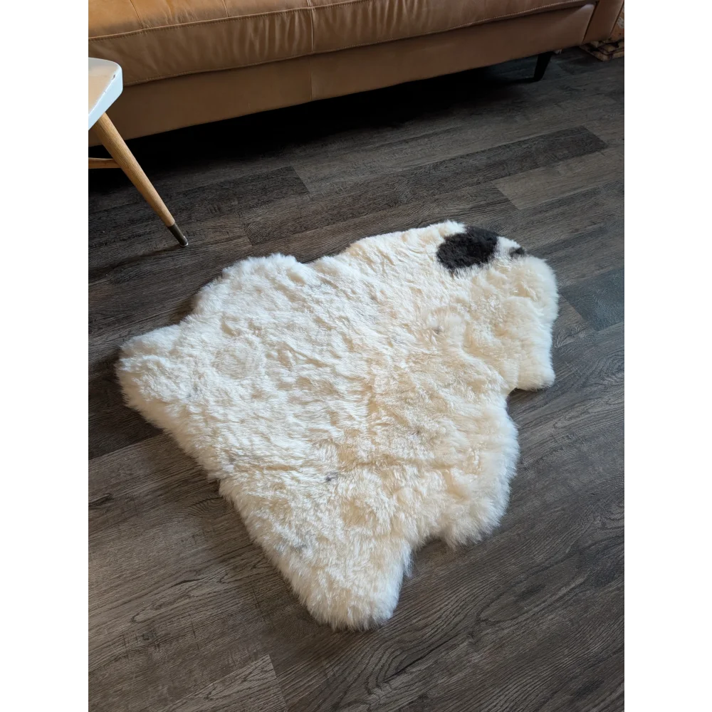 A fluffy white icelandic sheepskin rug with short wool and a black spot on dark wood flooring spot18 medium