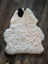 A plush white icelandic sheepskin with a black patch featuring medium short wool on dark wood floor
